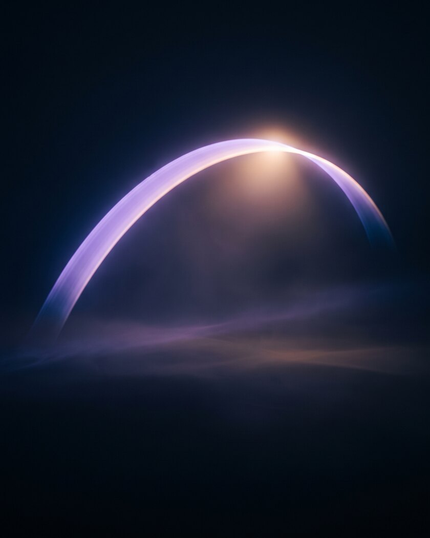 A soft violet arc of light curving through darkness, brightening to a warm amber point at its crest, with low mist drifting beneath it.